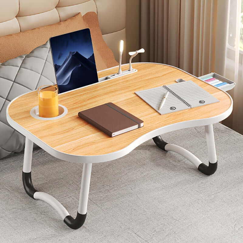 Portable laptop bed table with drink holder, LED light, notebook, and tablet on a bed.