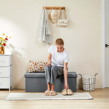 Woman choosing slippers while sitting on a stylish storage ottoman bench in a cozy entryway.