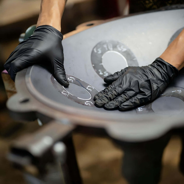 Person wearing disposable nitrile gloves for safety while handling a metallic workpiece.