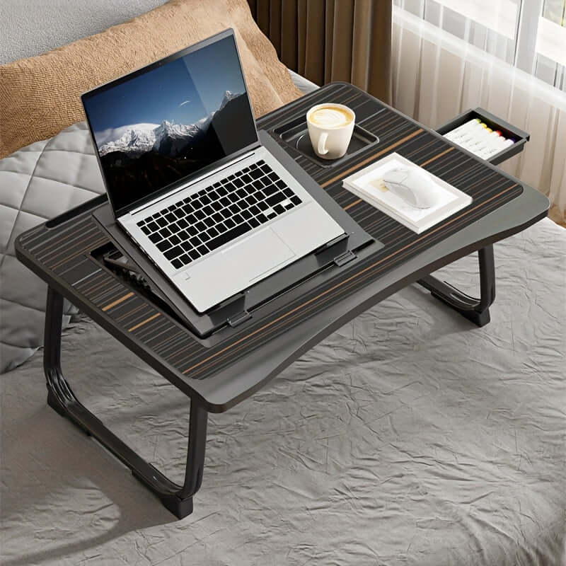 Portable laptop bed table with a laptop, coffee cup, and stationary on a bed.