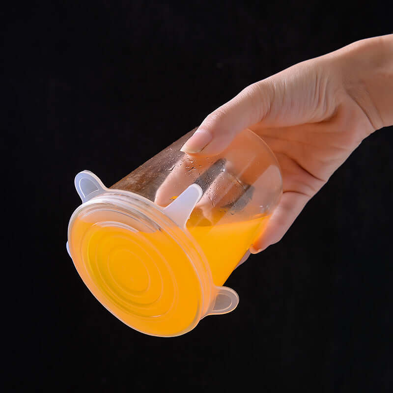 Silicone food storage covers securely sealing a cup filled with orange juice, demonstrating its effectiveness.