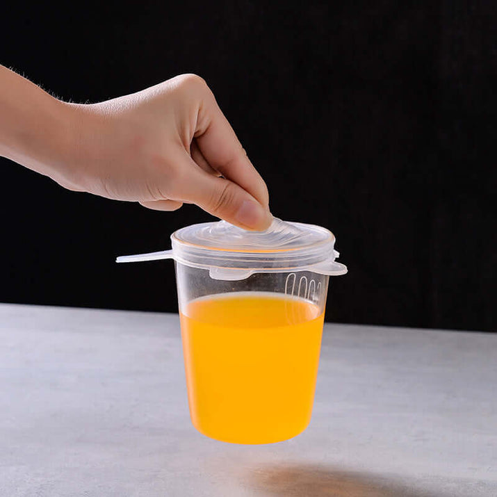 Hand placing silicone food storage covers on a container with bright orange liquid.