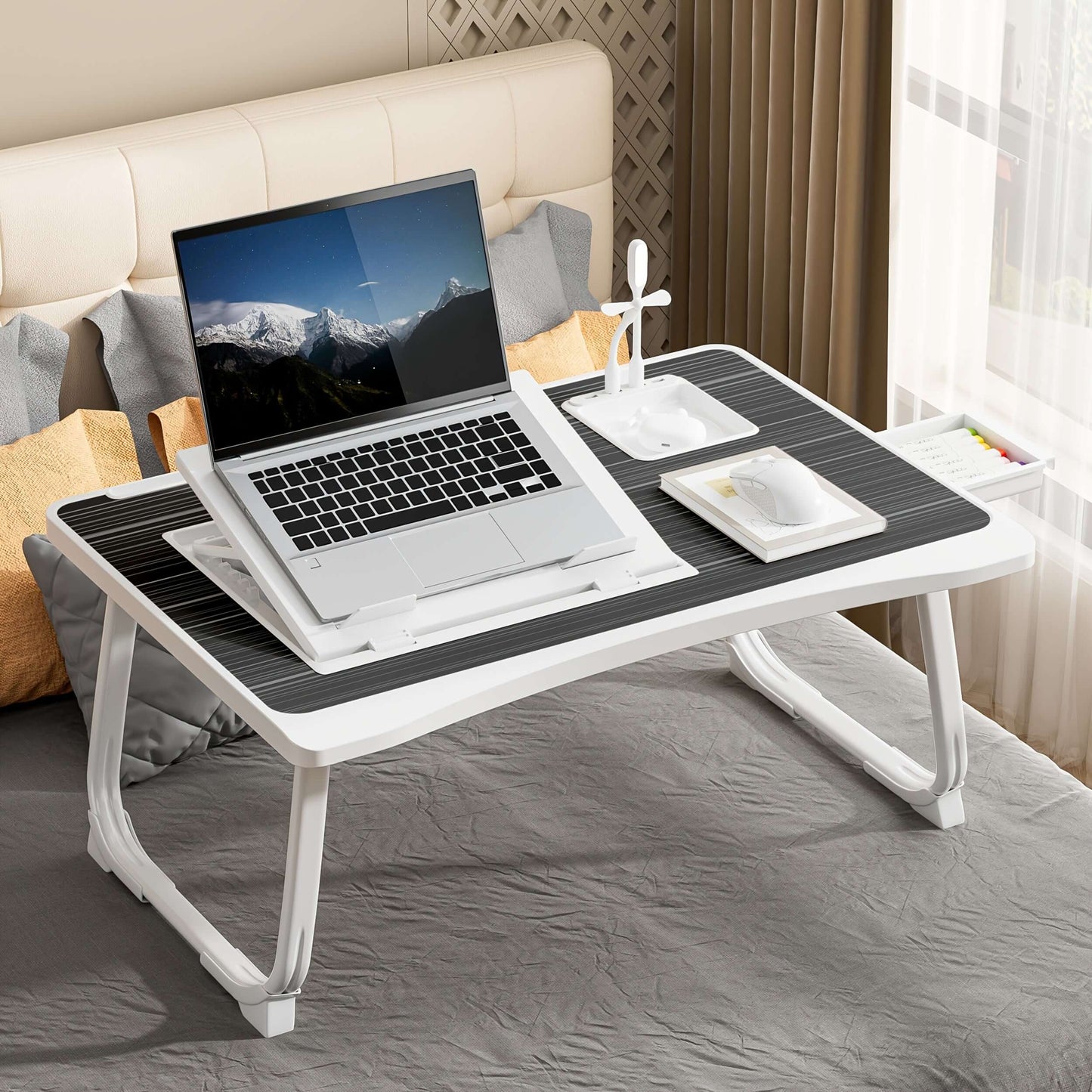 portable laptop bed table with laptop, notebook, and stationery on a bed.
