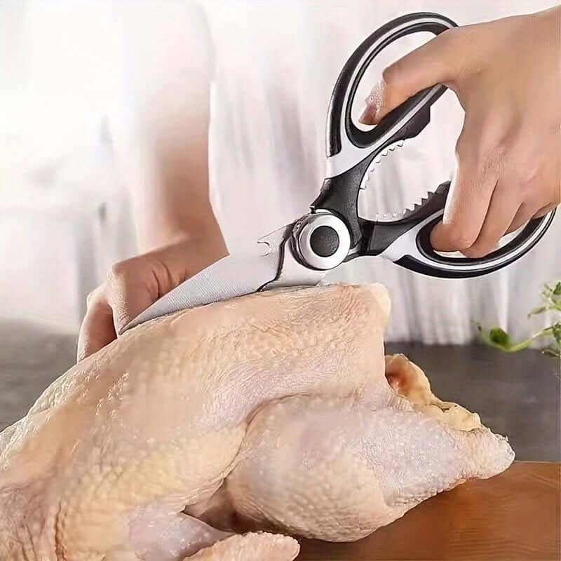 Person using durable stainless steel kitchen shears to cut a chicken on a kitchen countertop.