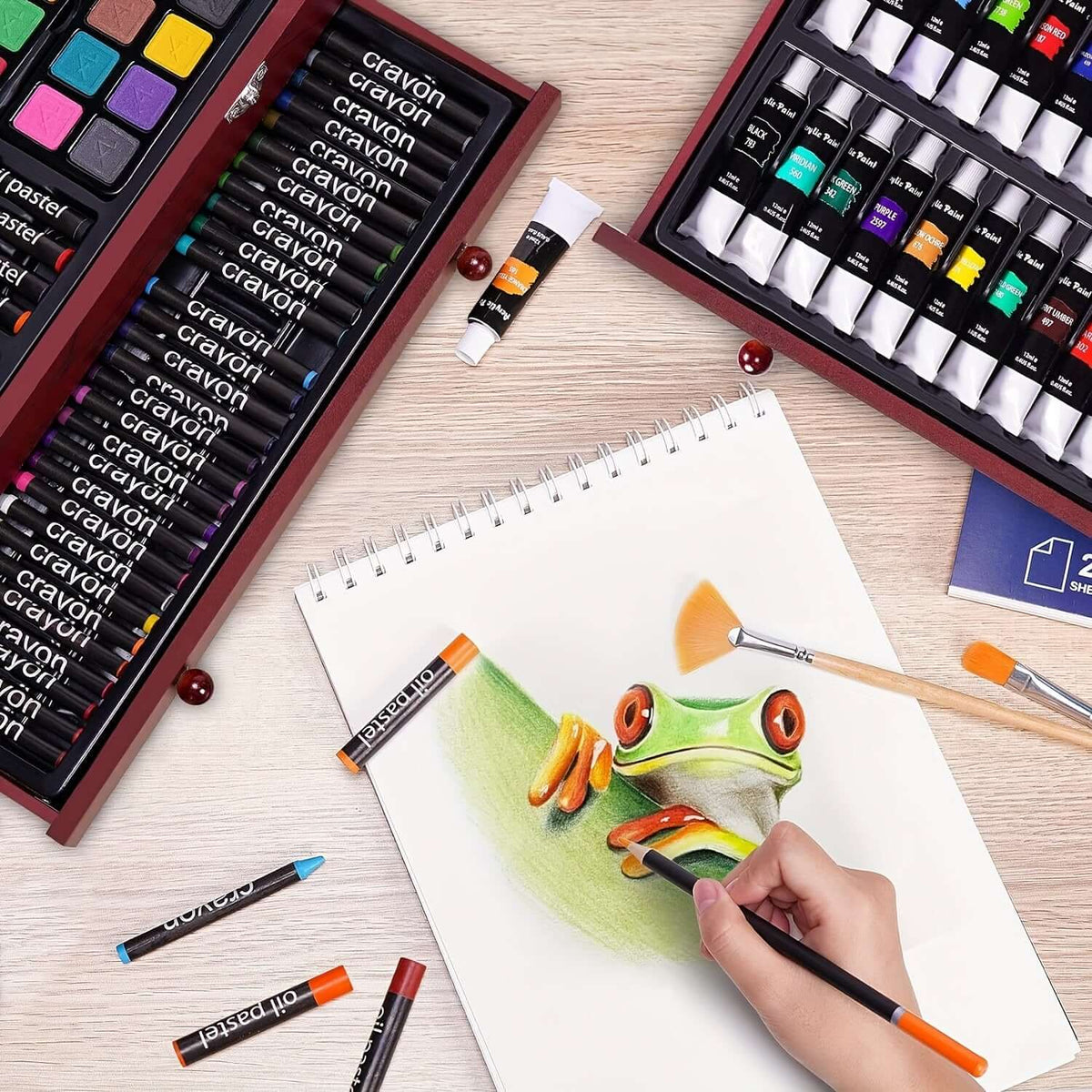 A workspace with PASAMIC non-toxic art supplies showing a hand drawing a colorful frog on sketch paper.