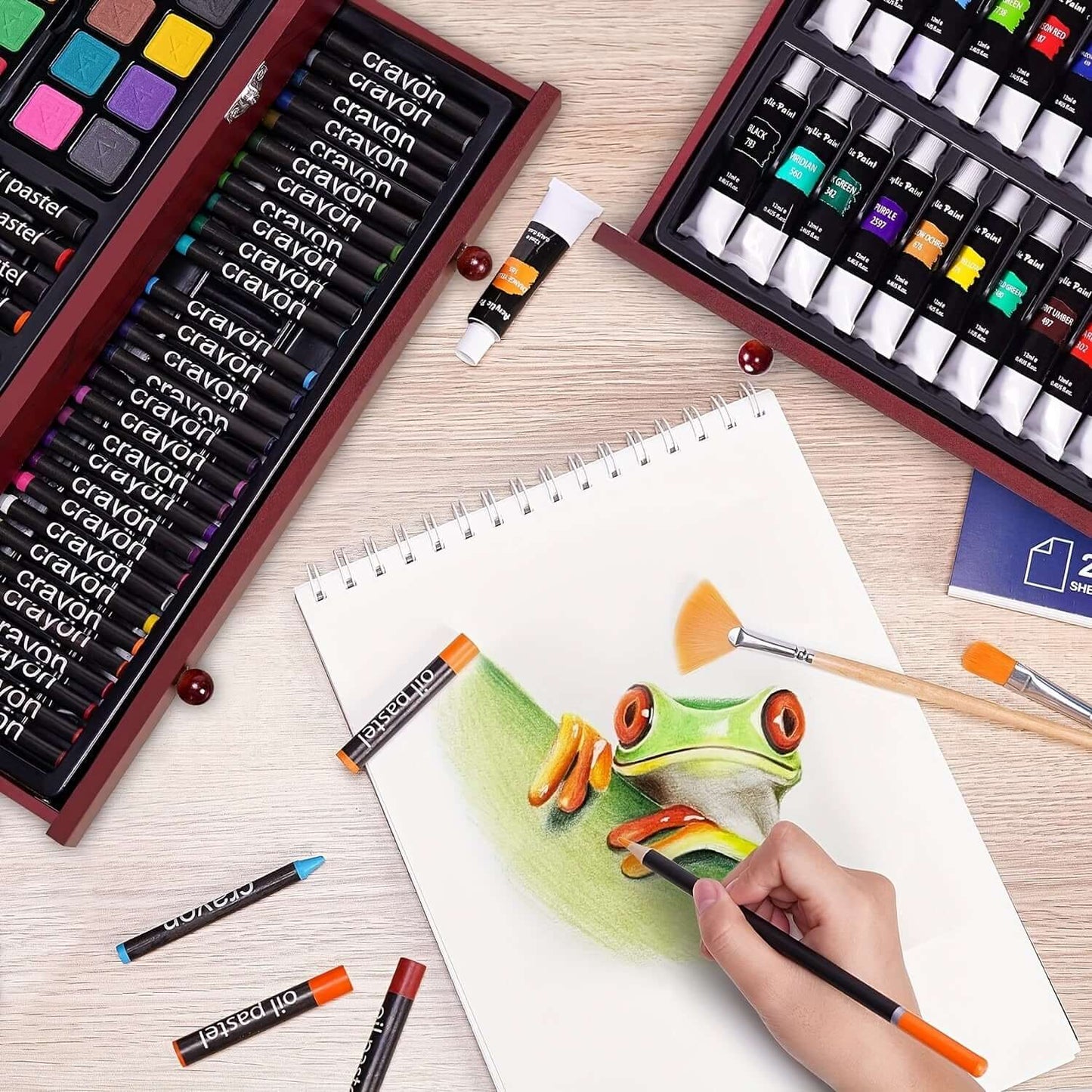 A workspace with PASAMIC non-toxic art supplies showing a hand drawing a colorful frog on sketch paper.