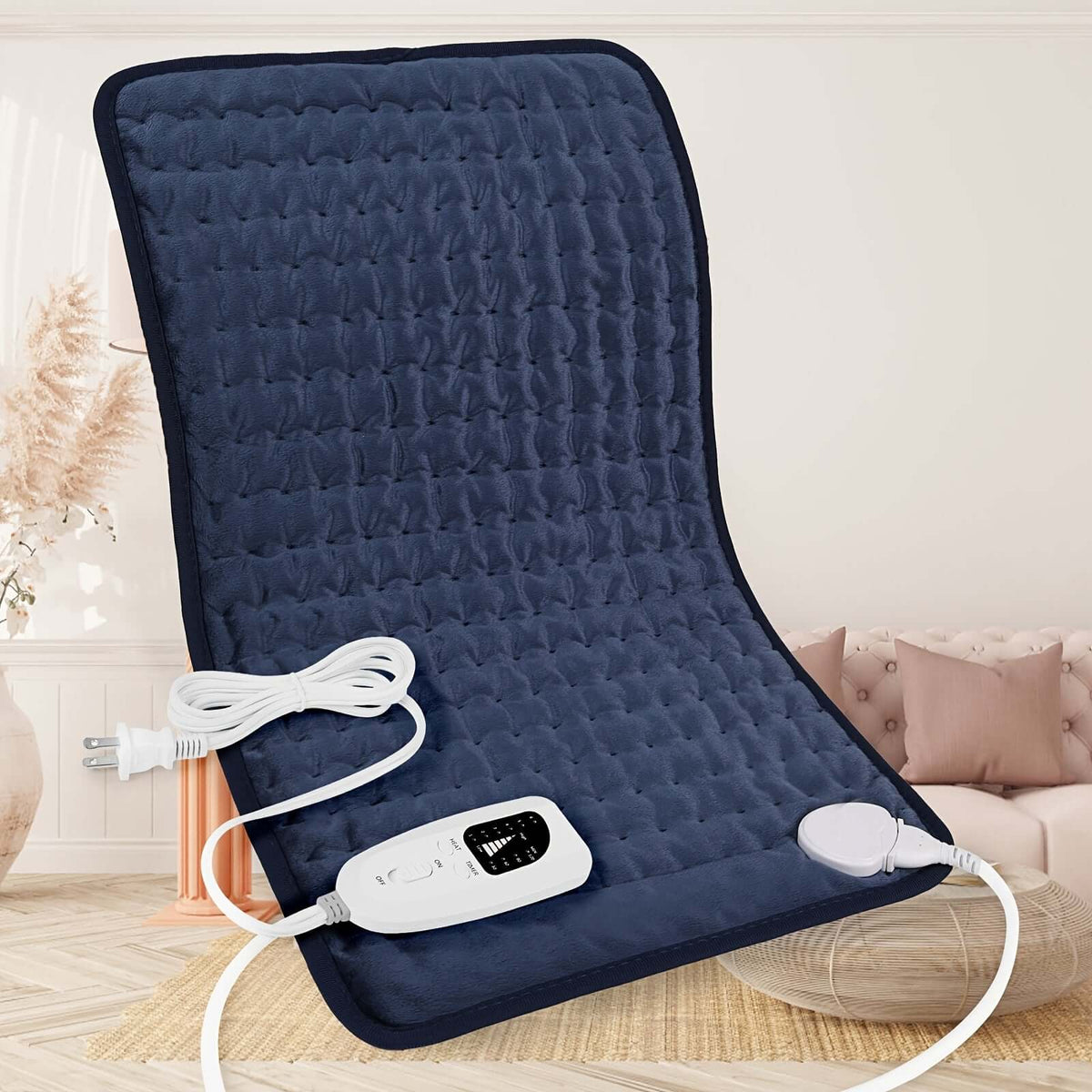 Extra large electric heating pad with controller on a comfortable couch in a cozy living room setting.