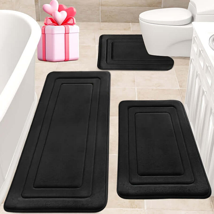 Memory foam bath mat set in black on a tile bathroom floor with a gift box nearby.