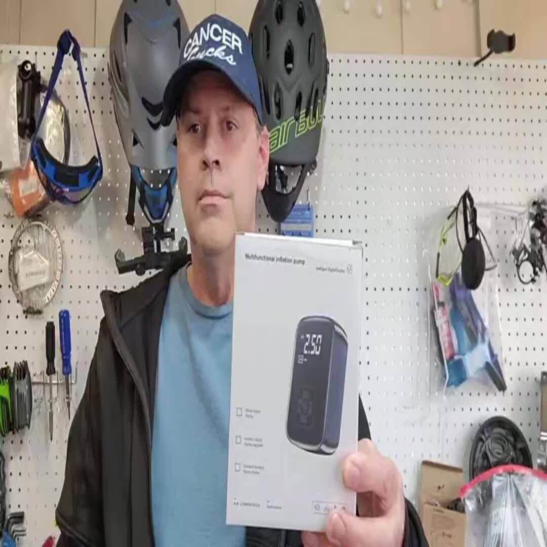 Man holding a portable tire inflator with digital display in a shop, showcasing its features and design.