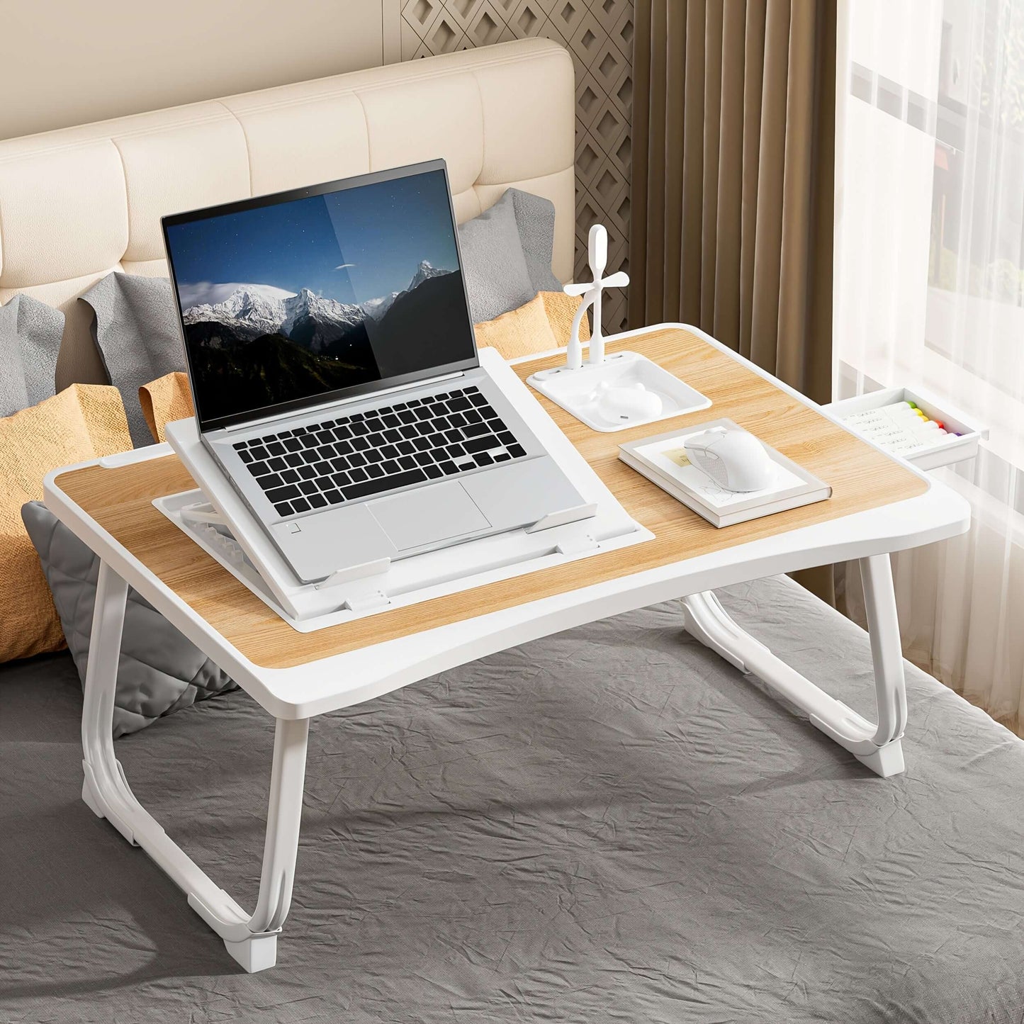 Portable laptop bed table with laptop and accessories on a bed in a cozy room.