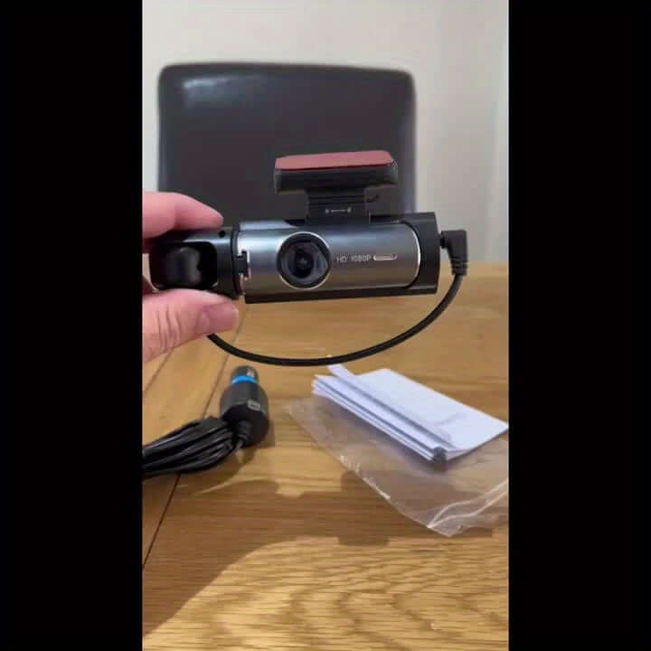 A hand holding a dual camera dash cam, showcasing its features and design on a wooden table.