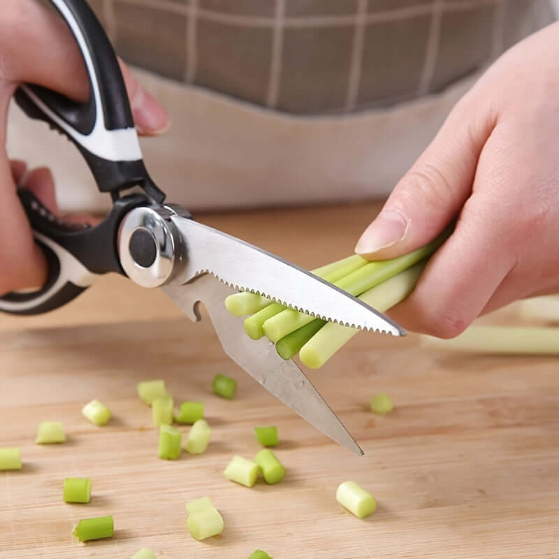 Person using durable stainless steel kitchen shears to cut green onions on a wooden cutting board.