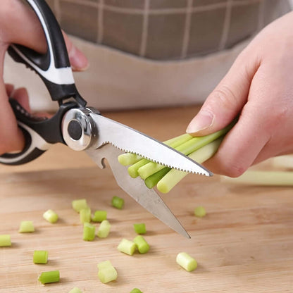 Person using durable stainless steel kitchen shears to cut green onions on a wooden cutting board.