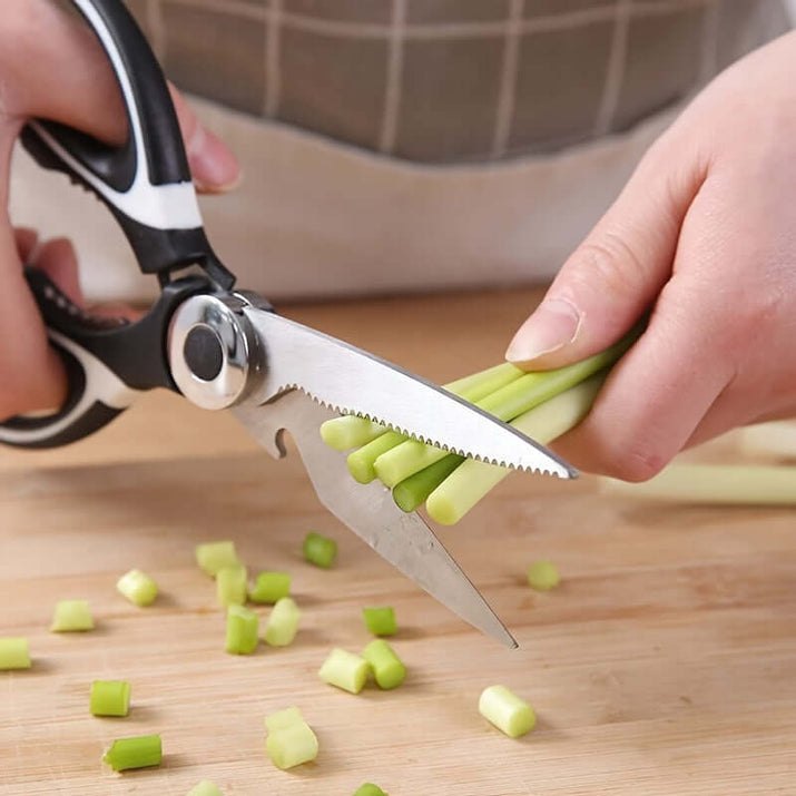 Person using durable stainless steel kitchen shears to cut green onions on a wooden cutting board.