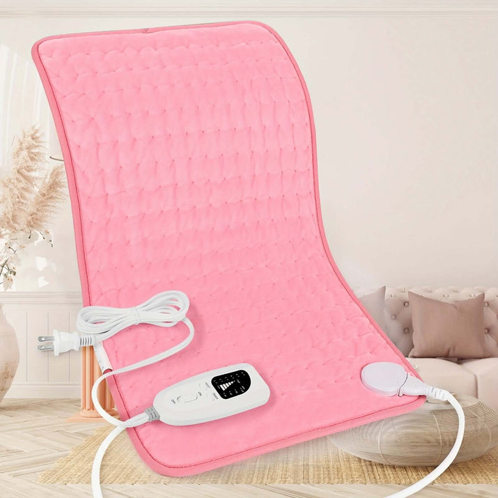 Extra large electric heating pad in pink color with control unit on a soft background.