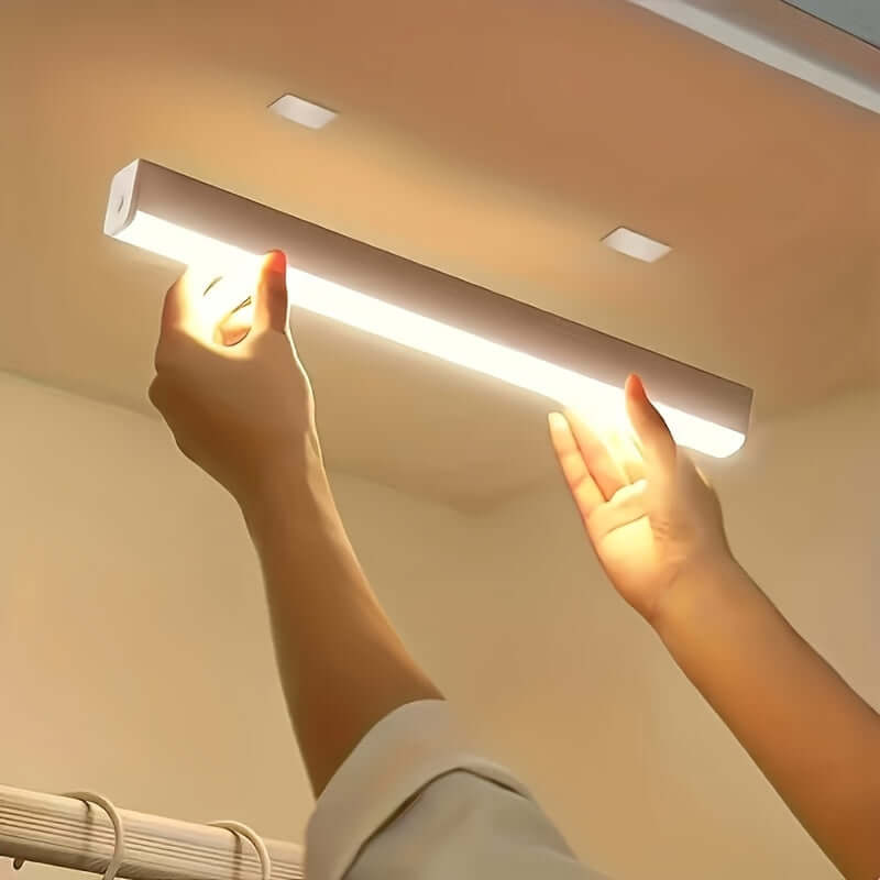 A person installing a wireless LED under cabinet light in a kitchen cabinet.