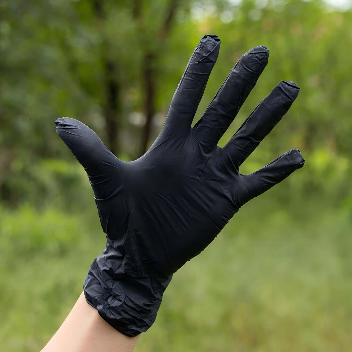 Disposable nitrile gloves for safety shown on a hand against a natural outdoor background.