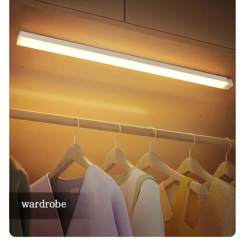wireless LED under cabinet light illuminating a wardrobe with hanging clothes.