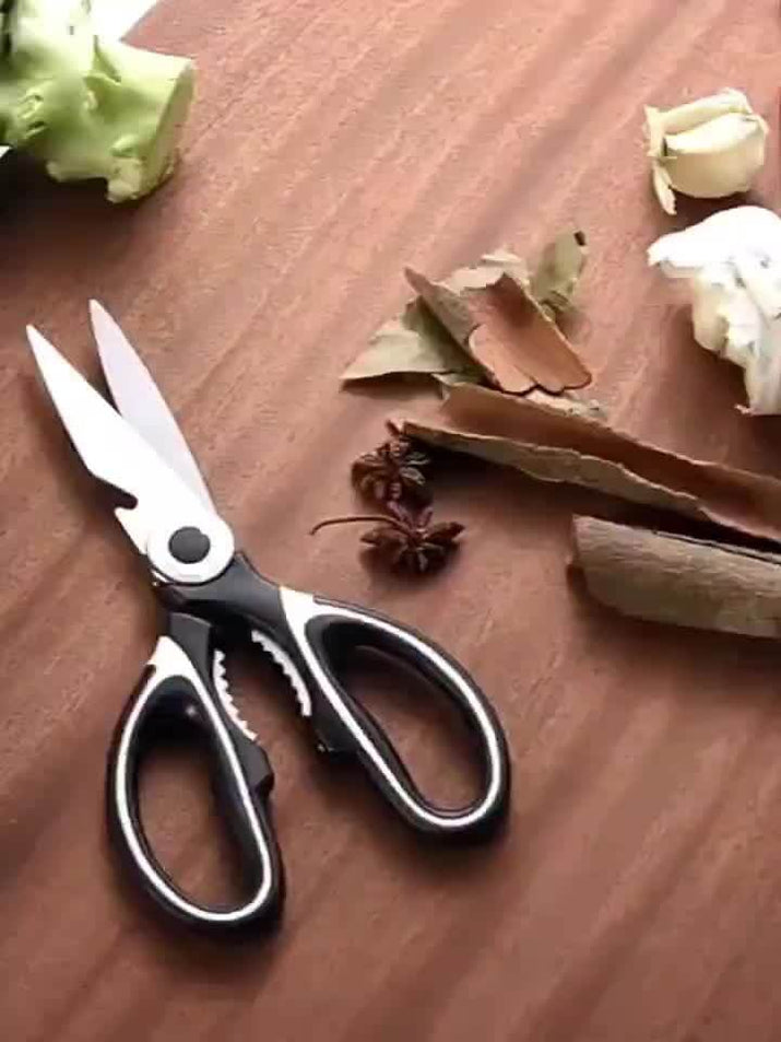 durable stainless steel kitchen shears on a wooden countertop with herbs and vegetables.